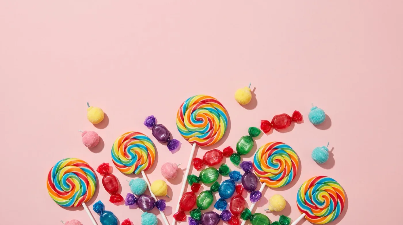 An overhead scattering of swirled lollipops and glossy coloured hard candies on a pastel pink surface