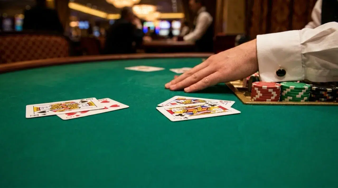 Two baccarat hands face up on a green casino table, king and nine against queen and jack, with the croupier's hand beside the chip tray