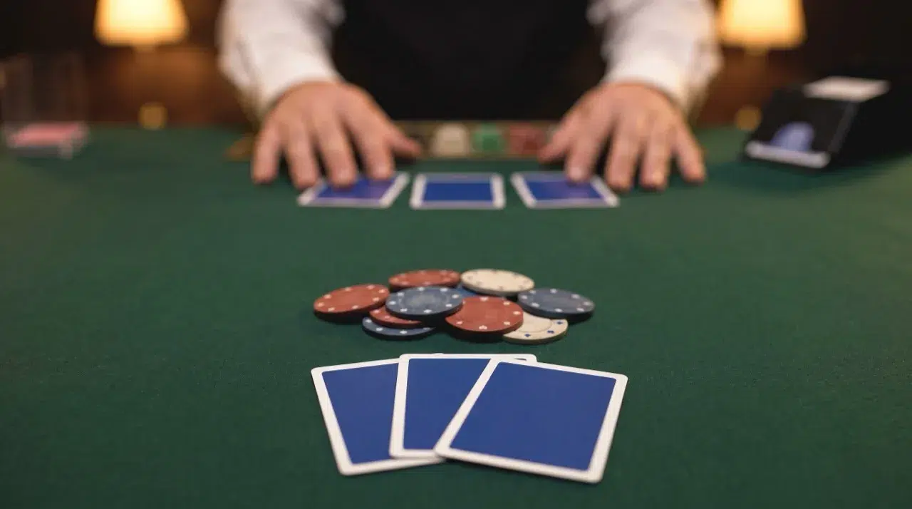 Three face-down cards and a pile of chips in front of the player, with the dealer's three cards behind, on a green card table